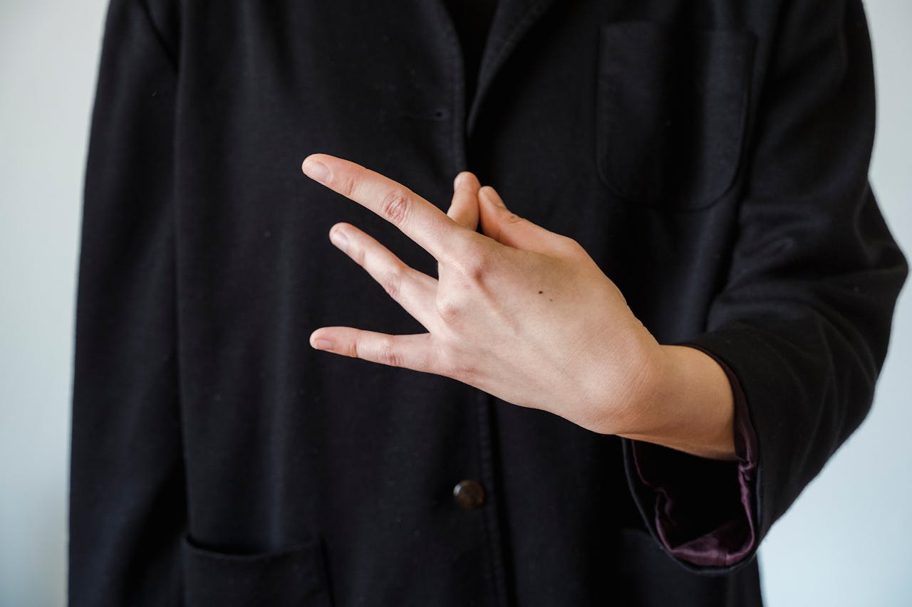 Mastering the First Impression: Your intriguing post title goes here A close-up of a hand making a gesture against a black coat background.
